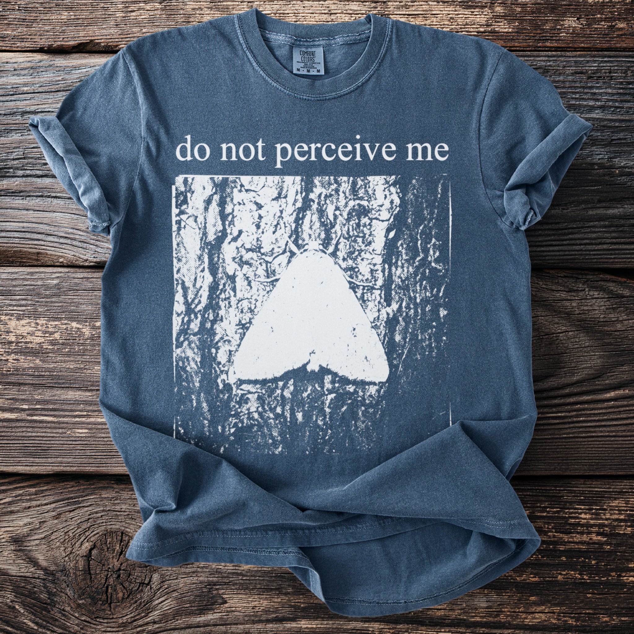 Blue t-shirt with white text "do not perceive me" and a moth graphic.