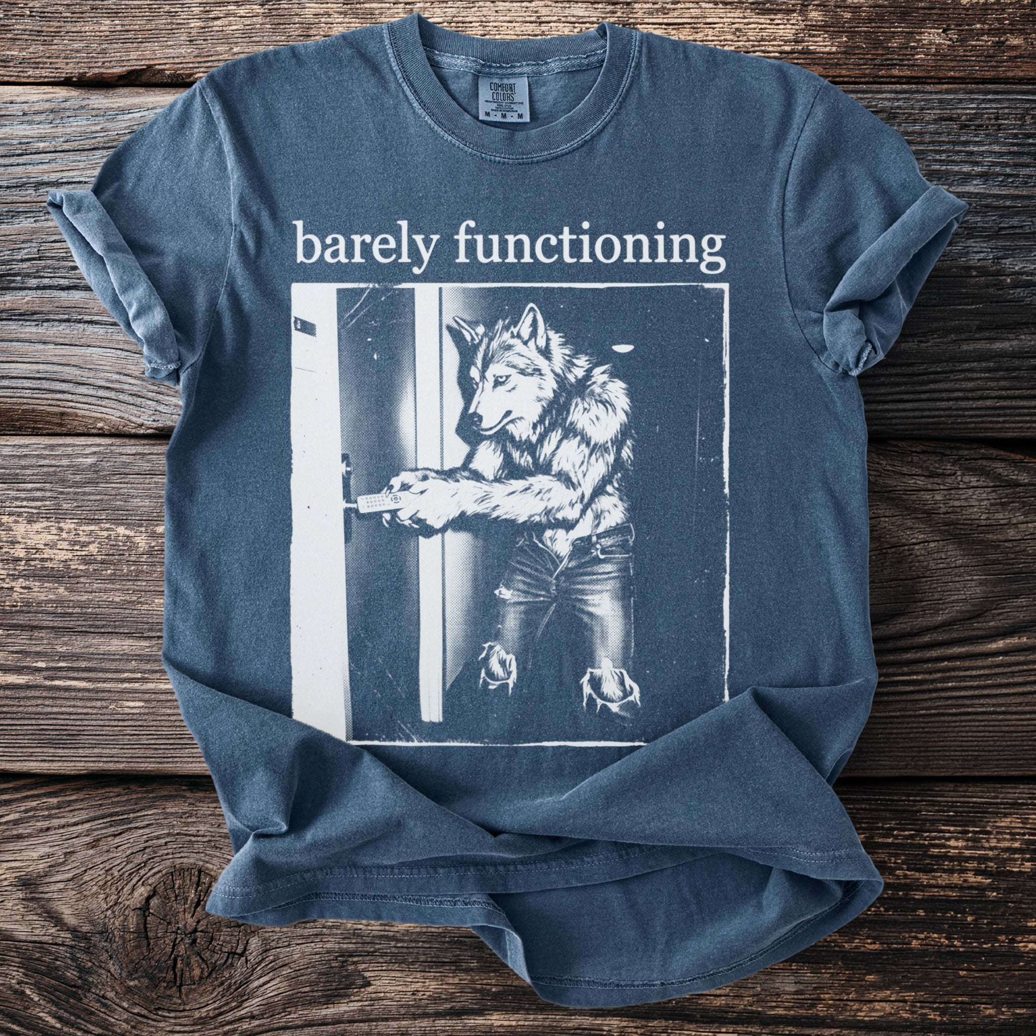 Blue t-shirt with white text "barely functioning" and a graphic of a wolf in jeans holding a remote.