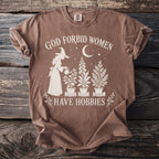 Brown t-shirt with graphic reading "God Forbid Women Have Hobbies" and witch watering plants.