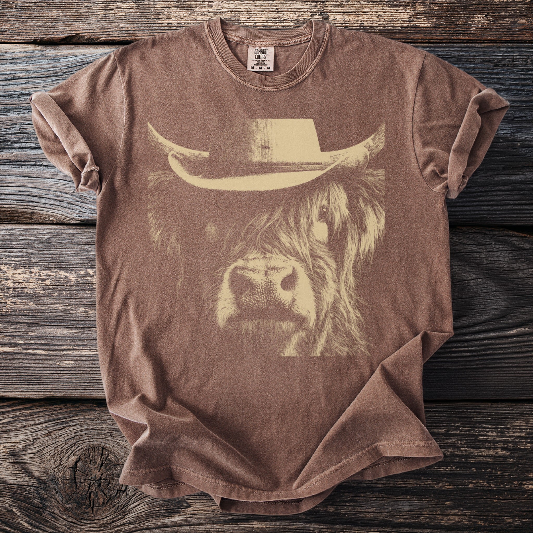 Brown t-shirt with a cream-colored line drawing of a highland cow wearing a cowboy hat.
