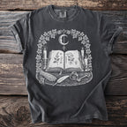 Dark gray t-shirt with a white occult design featuring an open book, moon, candles, and herbs.