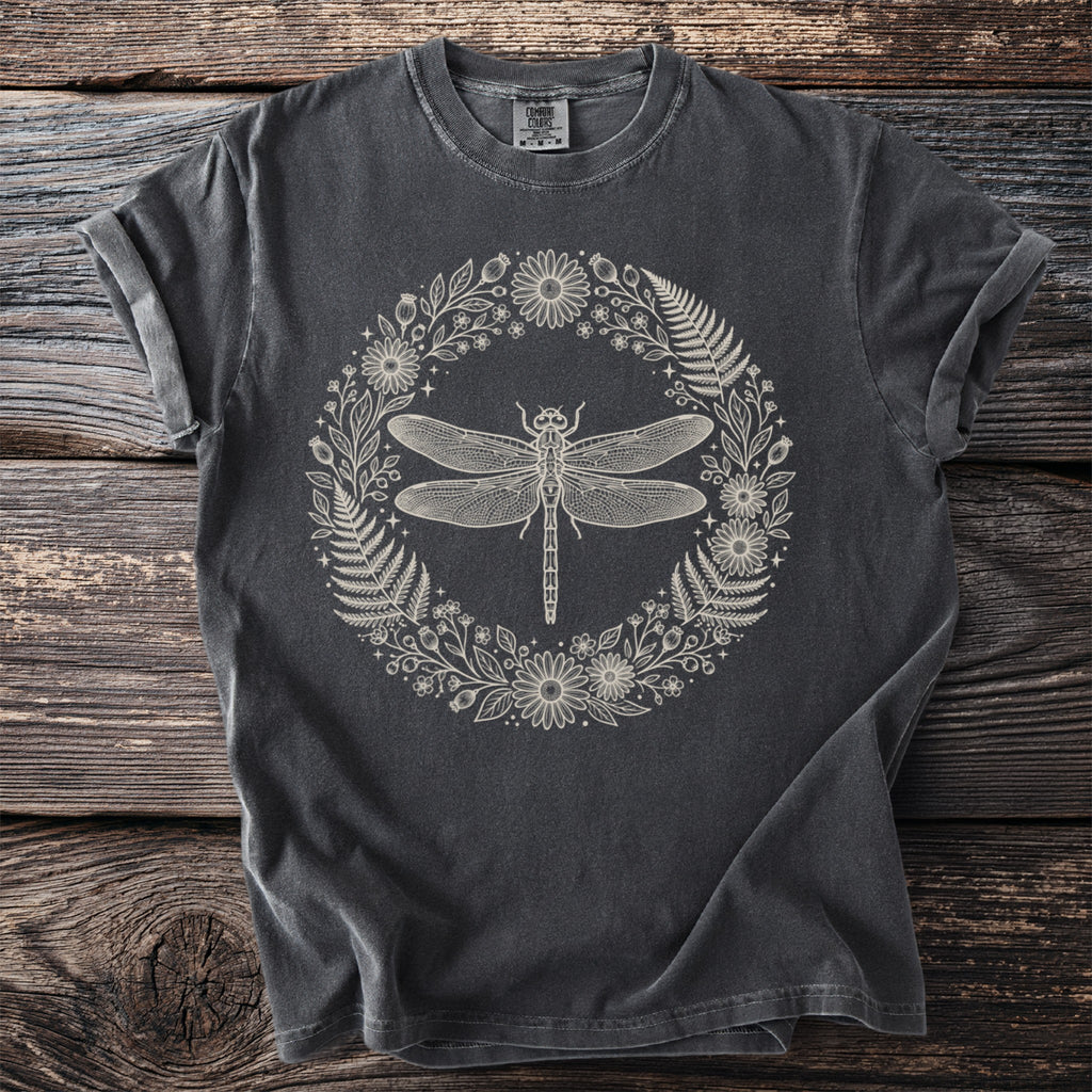 Dark grey t-shirt with line art of a dragonfly within a floral and fern wreath.
