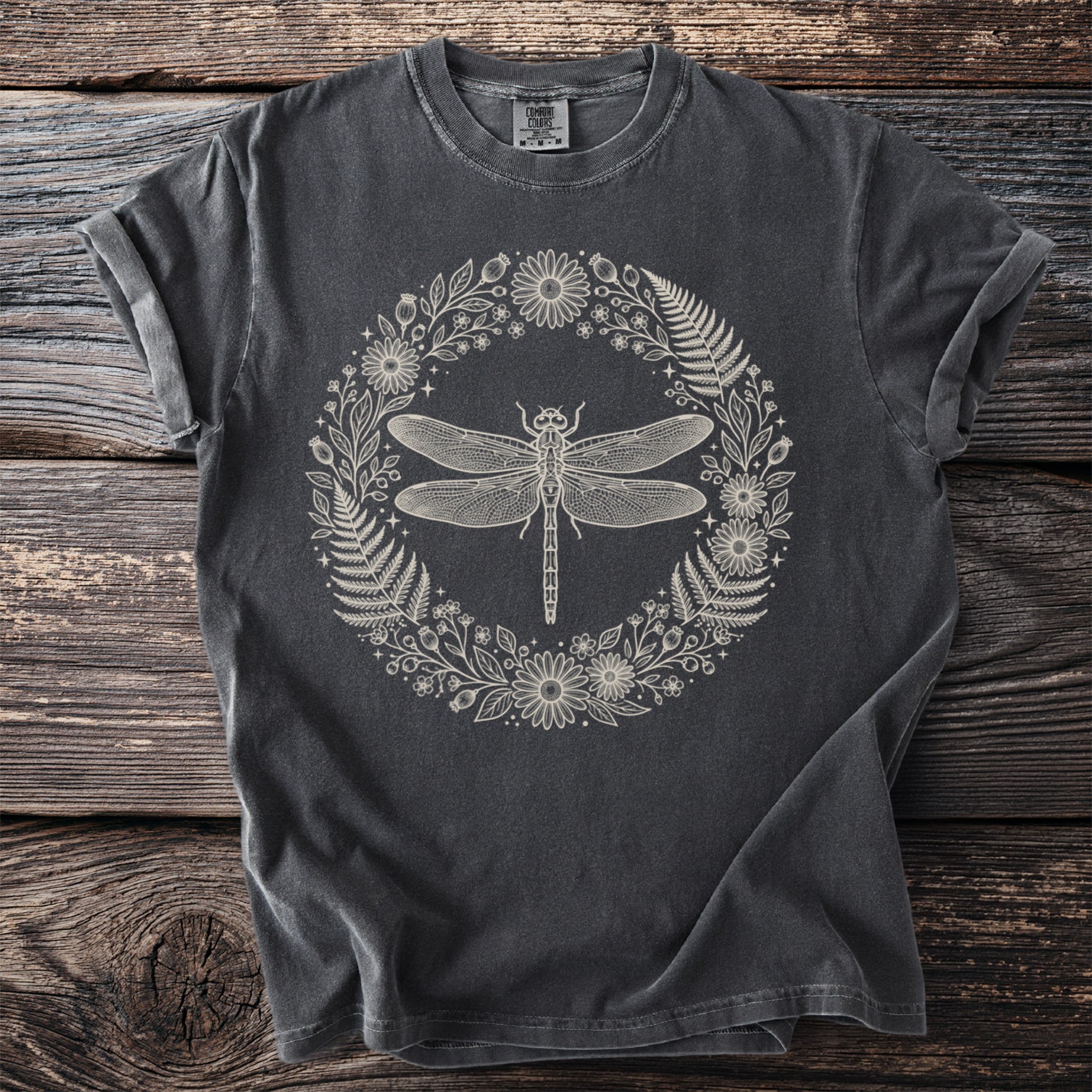 Dark grey t-shirt with line art of a dragonfly within a floral and fern wreath.