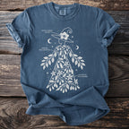 Blue t-shirt with witch design featuring botanical illustrations and text labels.