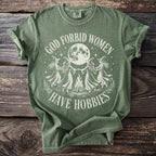 Green t-shirt with "God Forbid Women Have Hobbies" text and witch design