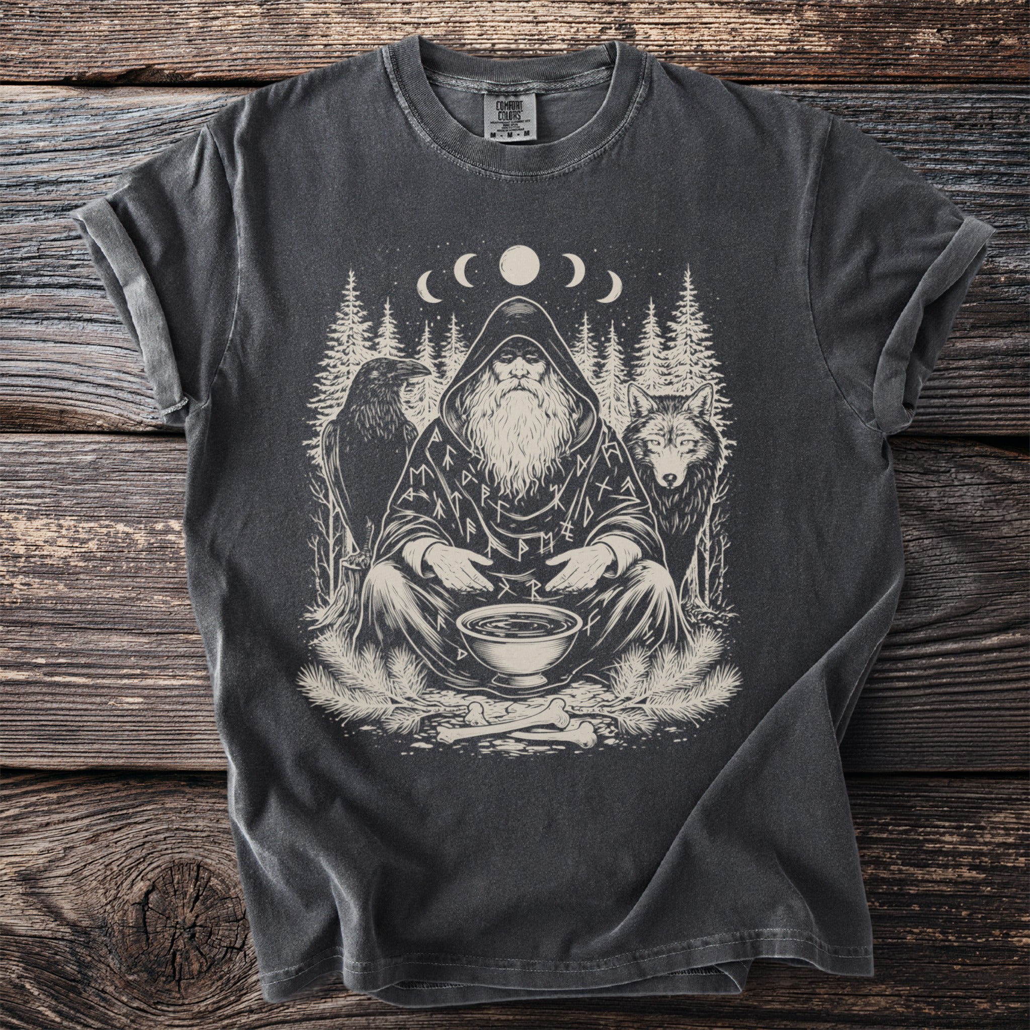 T-shirt graphic shows a seated wizard surrounded by a wolf, raven, pine trees, and moon phases.