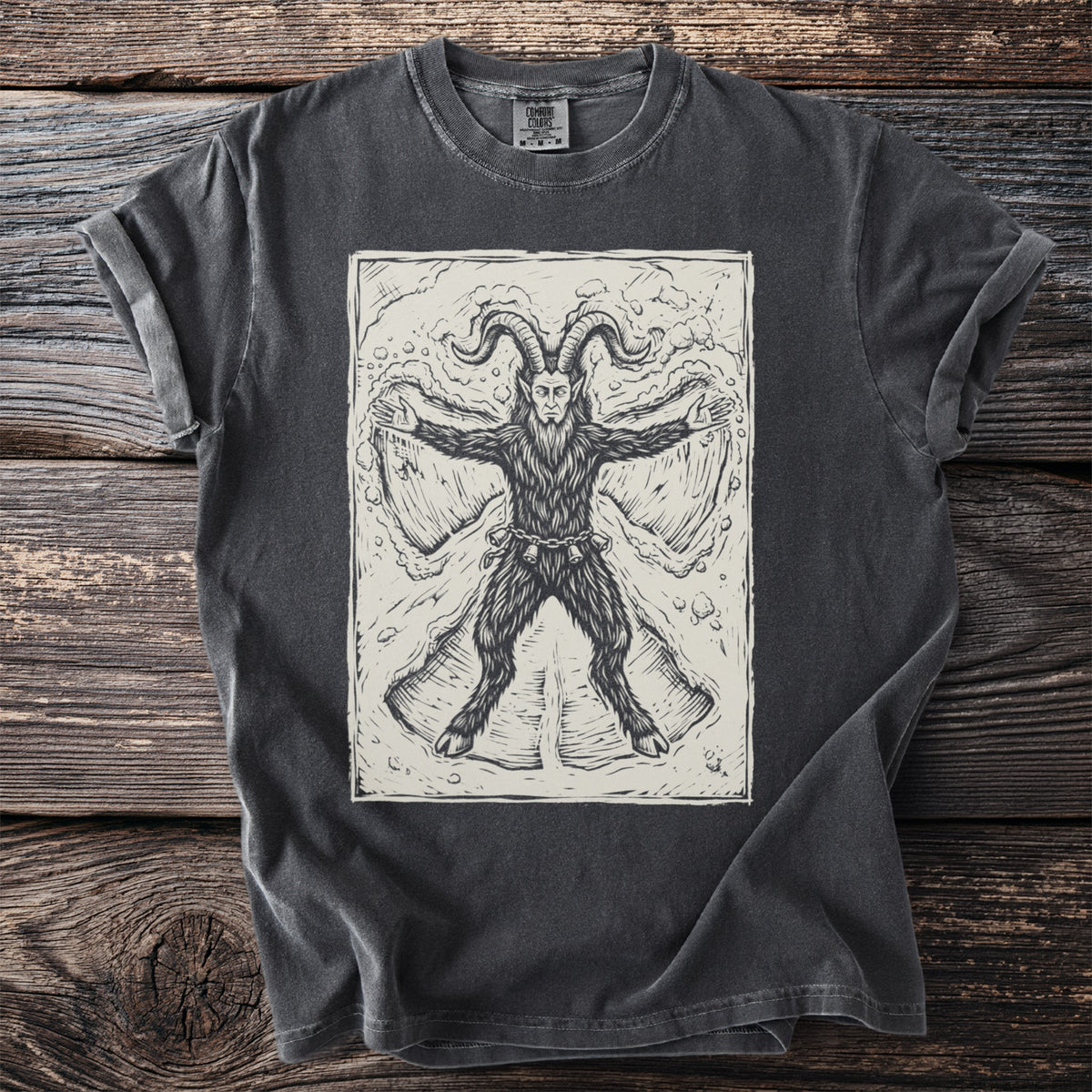 Pepper gray t-shirt with a cream folk-cut print: Krampus lies flat on his back in fresh snow, arms and hooves spread, making a snow angel.