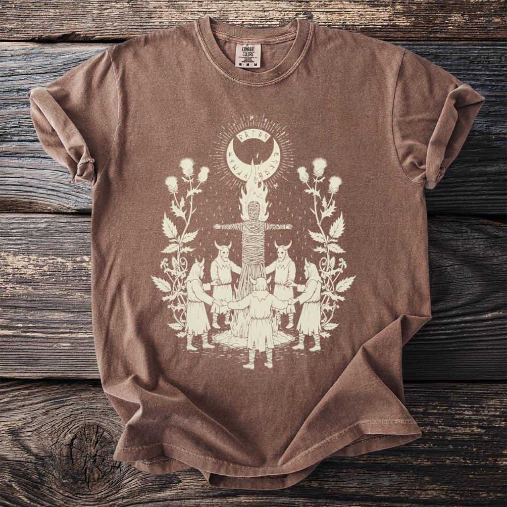Brown t-shirt with a cream graphic of a ritualistic scene with people and a figure on a pyre.