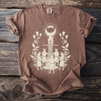 Brown t-shirt with a cream graphic of a ritualistic scene with people and a figure on a pyre.