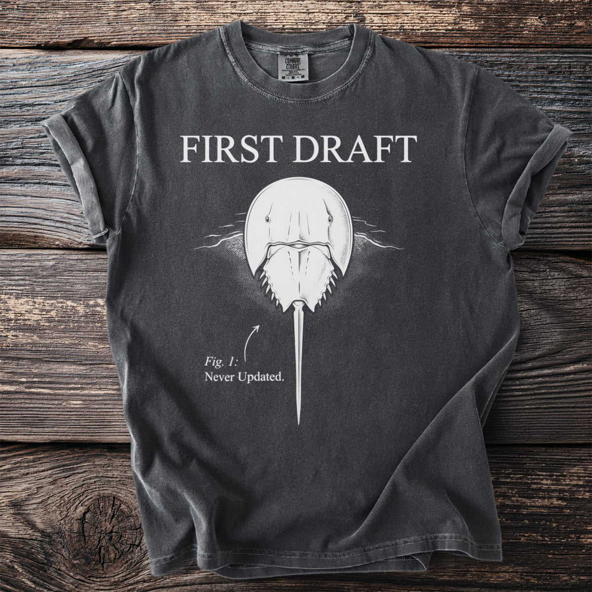 Dark grey t-shirt with "FIRST DRAFT" above a horseshoe crab labeled "Fig. 1: Never Updated."