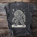 Pepper gray t-shirt with a cream folk-cut print: a hunched werewolf, teeth bared and claws out, stands in the snow under a crescent moon.