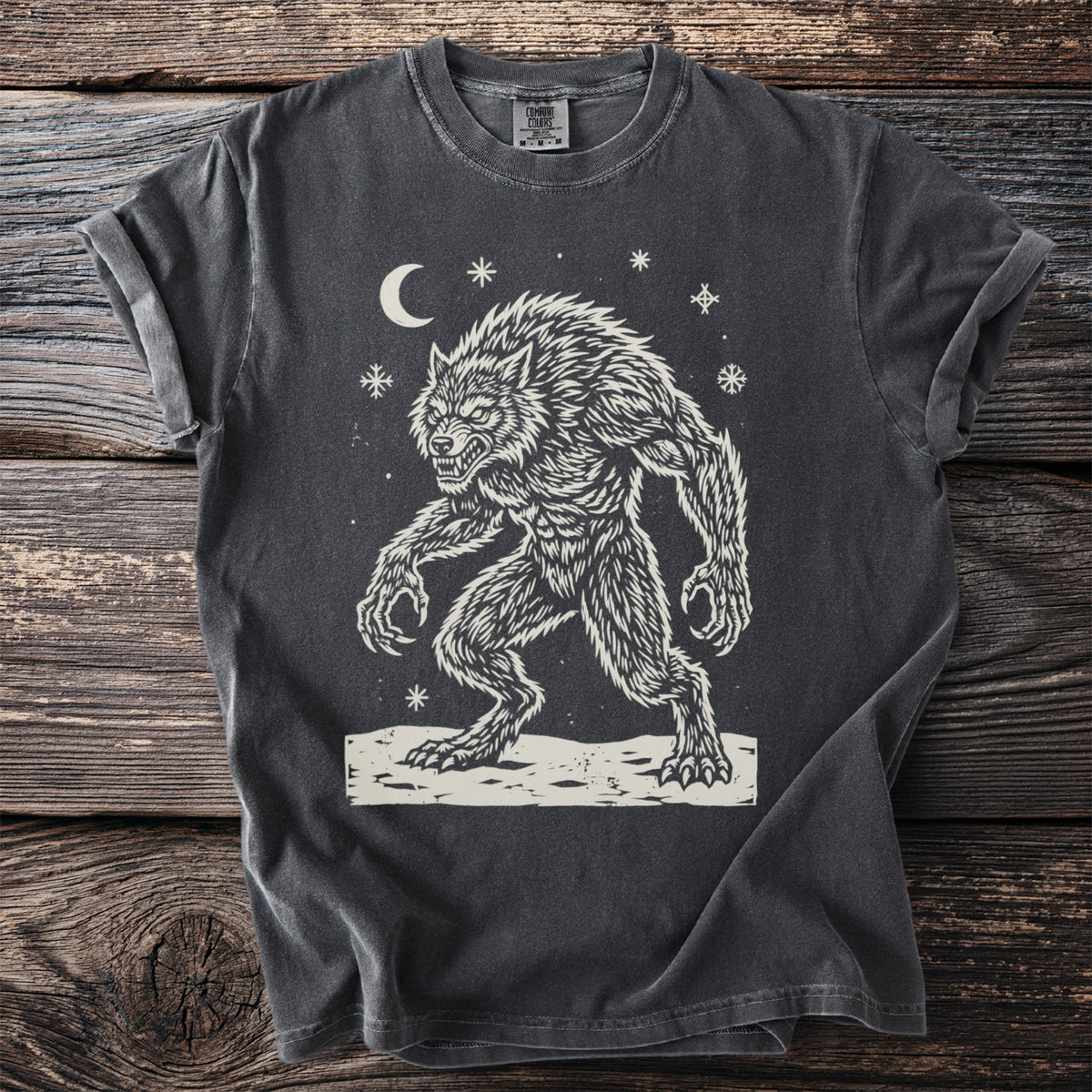 Pepper gray t-shirt with a cream folk-cut print: a hunched werewolf, teeth bared and claws out, stands in the snow under a crescent moon.