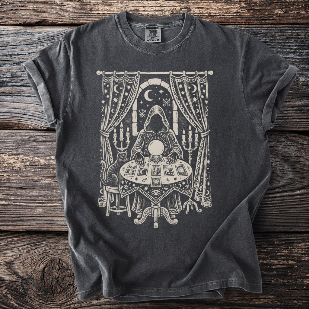 T-shirt graphic of a figure by a crystal ball, tarot cards, and a cat.