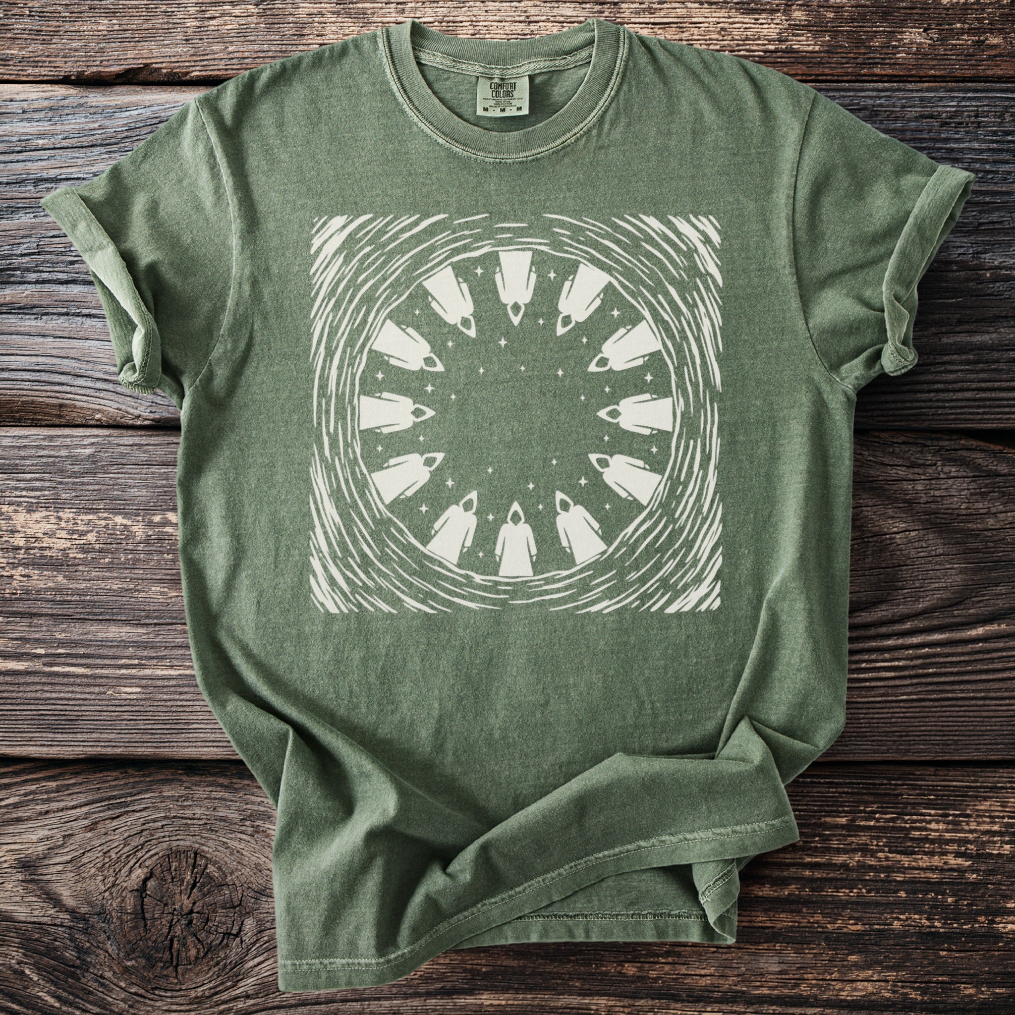 Green t-shirt with cream circular graphic of cloaked figures and stars.