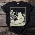 Black t-shirt with a line drawing of a cat smoking a cigarette next to plants and cans.