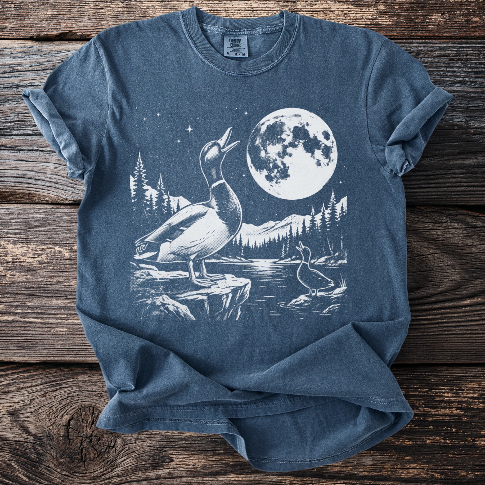 Two ducks in a white graphic on a blue t-shirt with a moonlit forest scene.