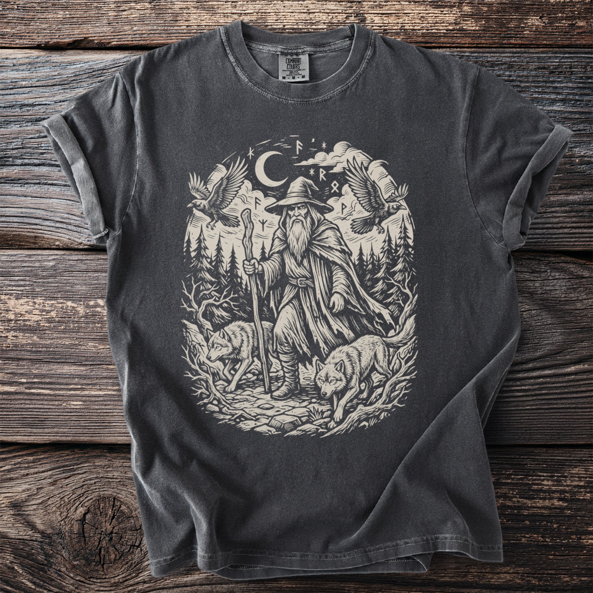 T-shirt graphic of a wizard with wolves and ravens in a forest under the moon.