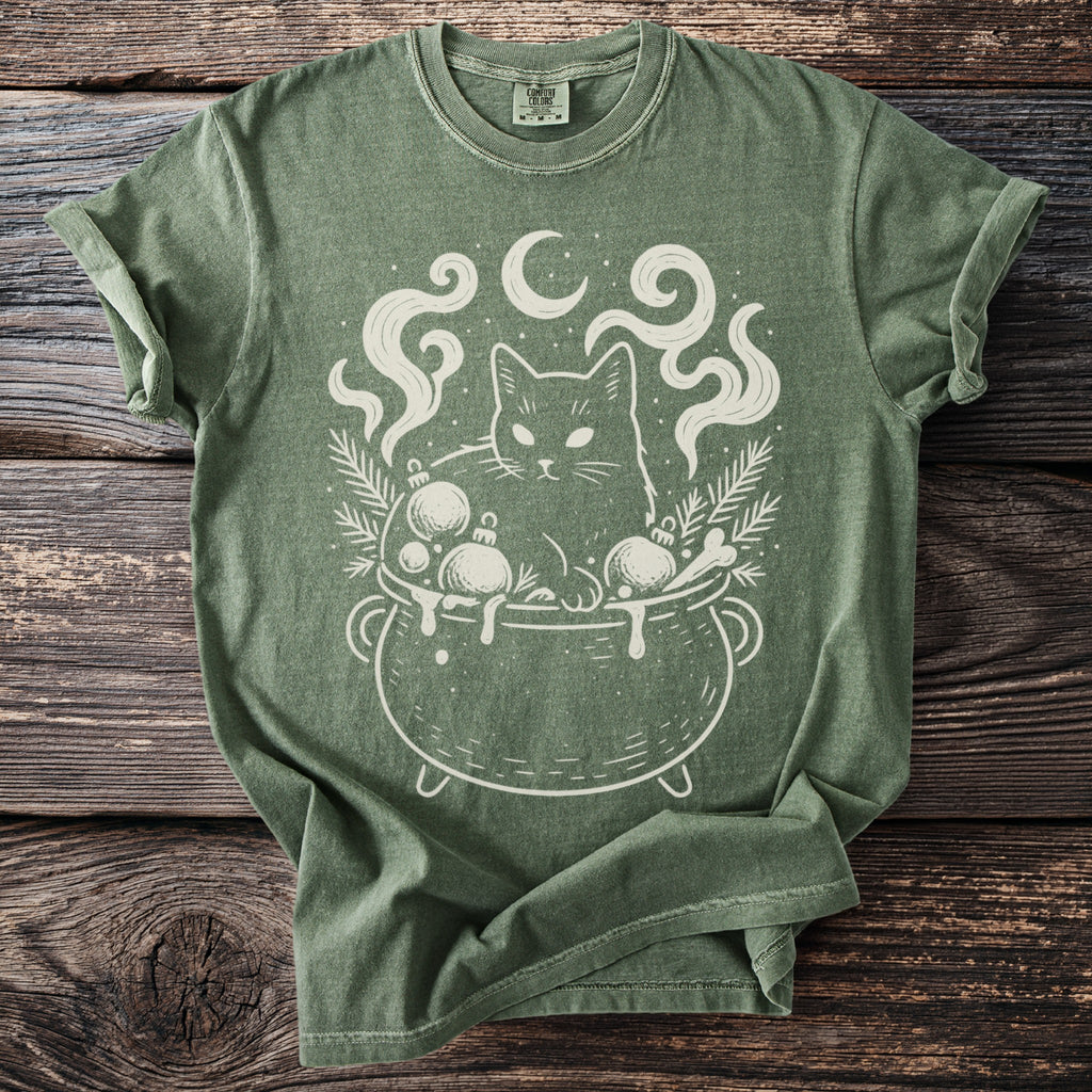 Green t-shirt with a white graphic of a cat in a cauldron with ornaments and smoke.