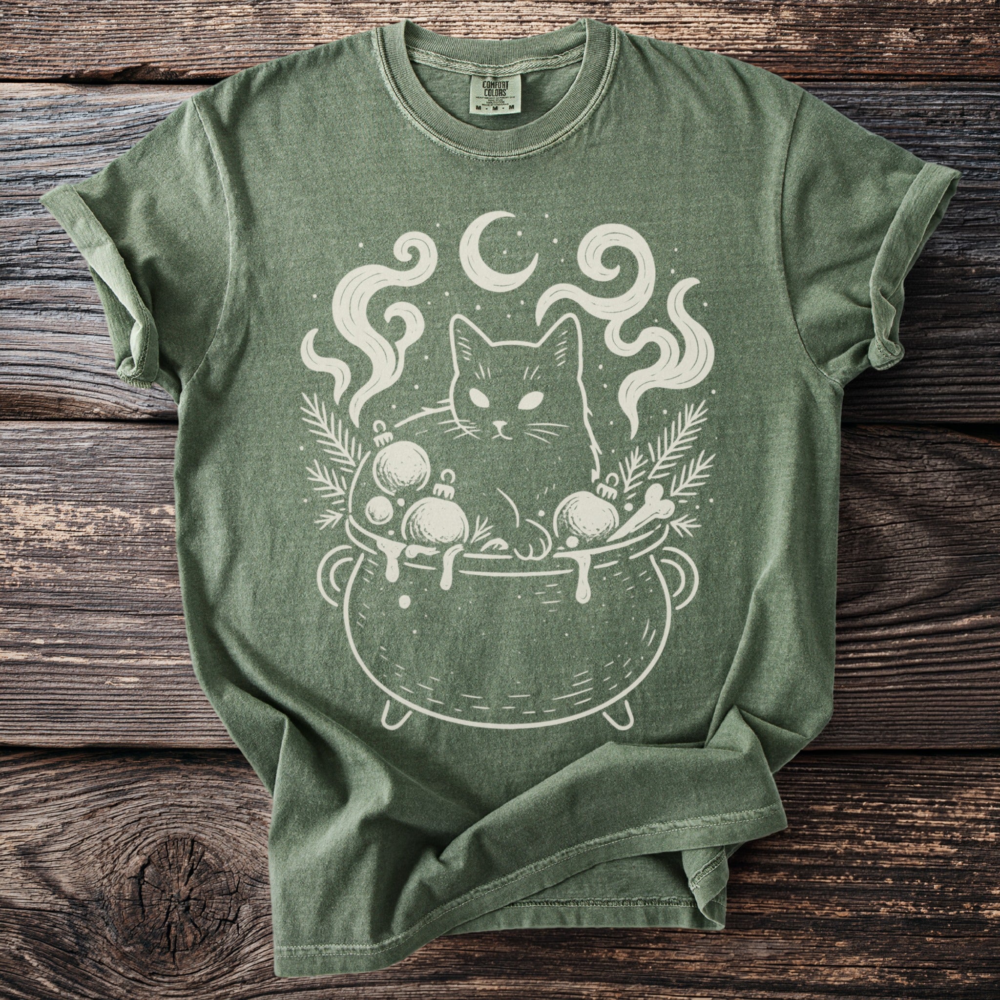 Green t-shirt with a white graphic of a cat in a cauldron with ornaments and smoke.