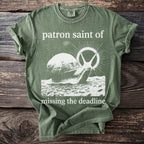 Olive green t-shirt with a snail graphic and text "patron saint of missing the deadline".