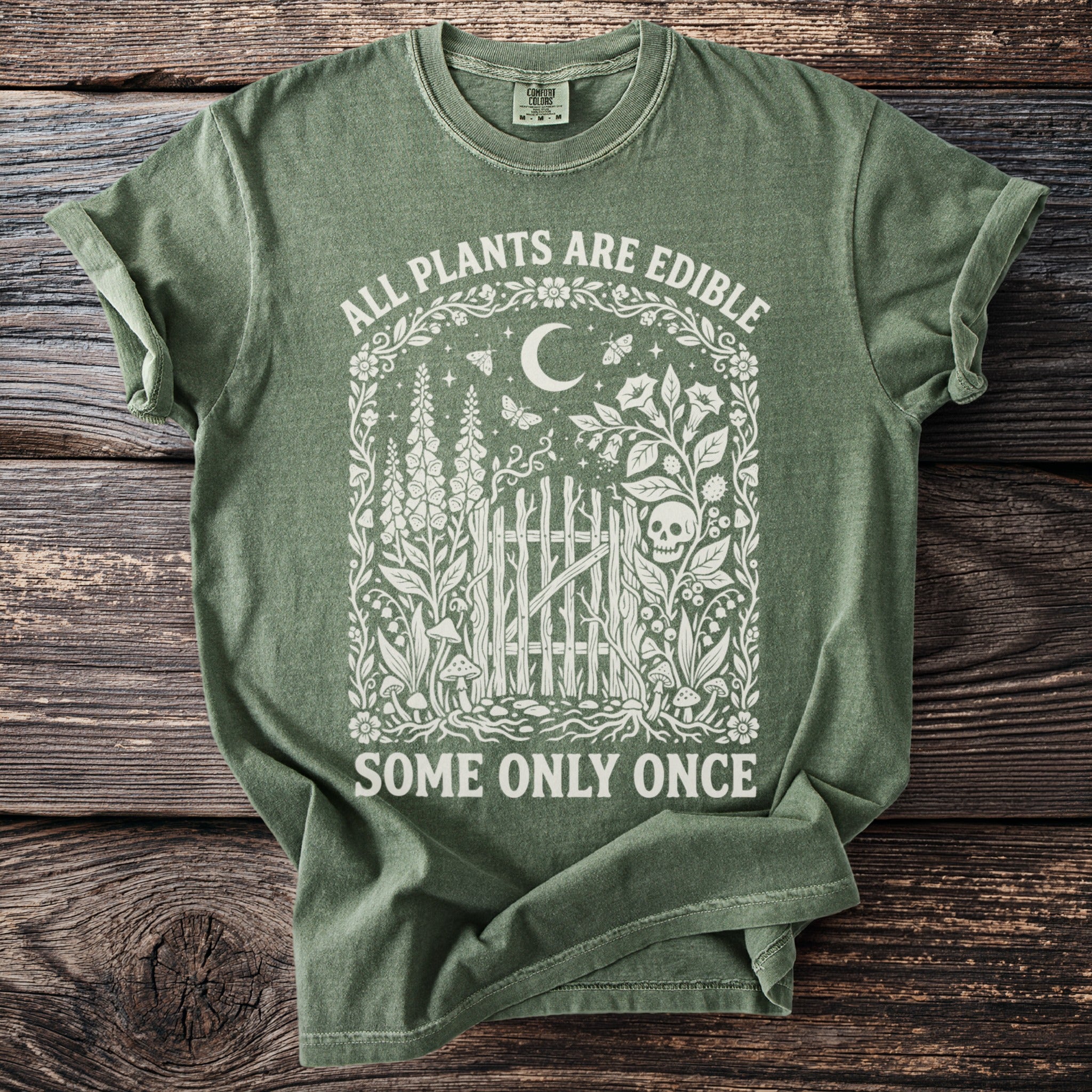 Green t-shirt with "ALL PLANTS ARE EDIBLE SOME ONLY ONCE" text and floral skull design.