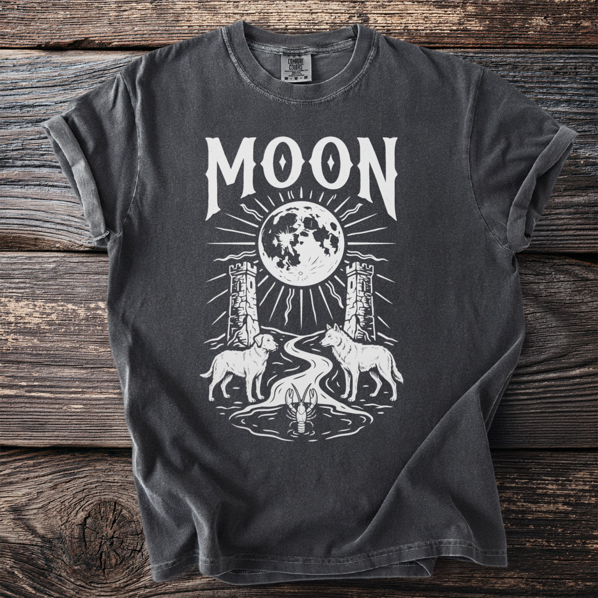 Dark grey t-shirt graphic with white text "MOON", a full moon, two towers, a dog, a wolf, a river, and a lobster.