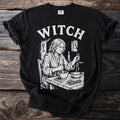Black t-shirt with "WITCH" text and a vintage illustration of a woman preparing ingredients.