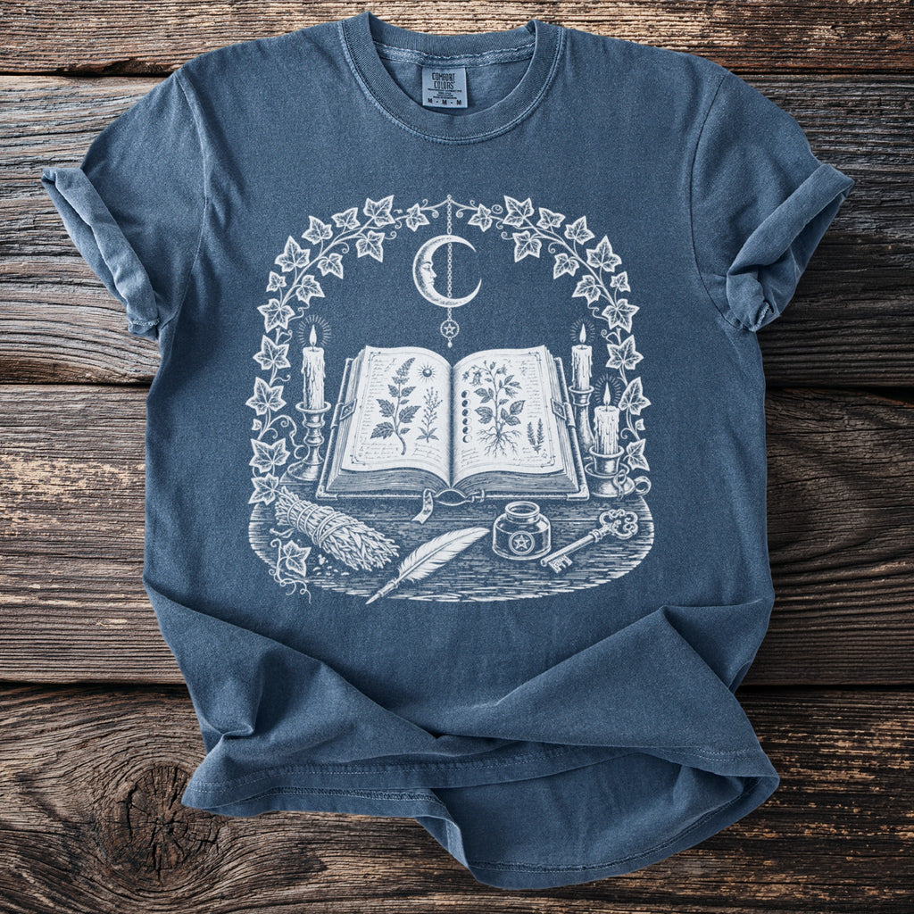 T-shirt with occult graphic: open book, candles, moon, quill, inkwell, key, and herbs.