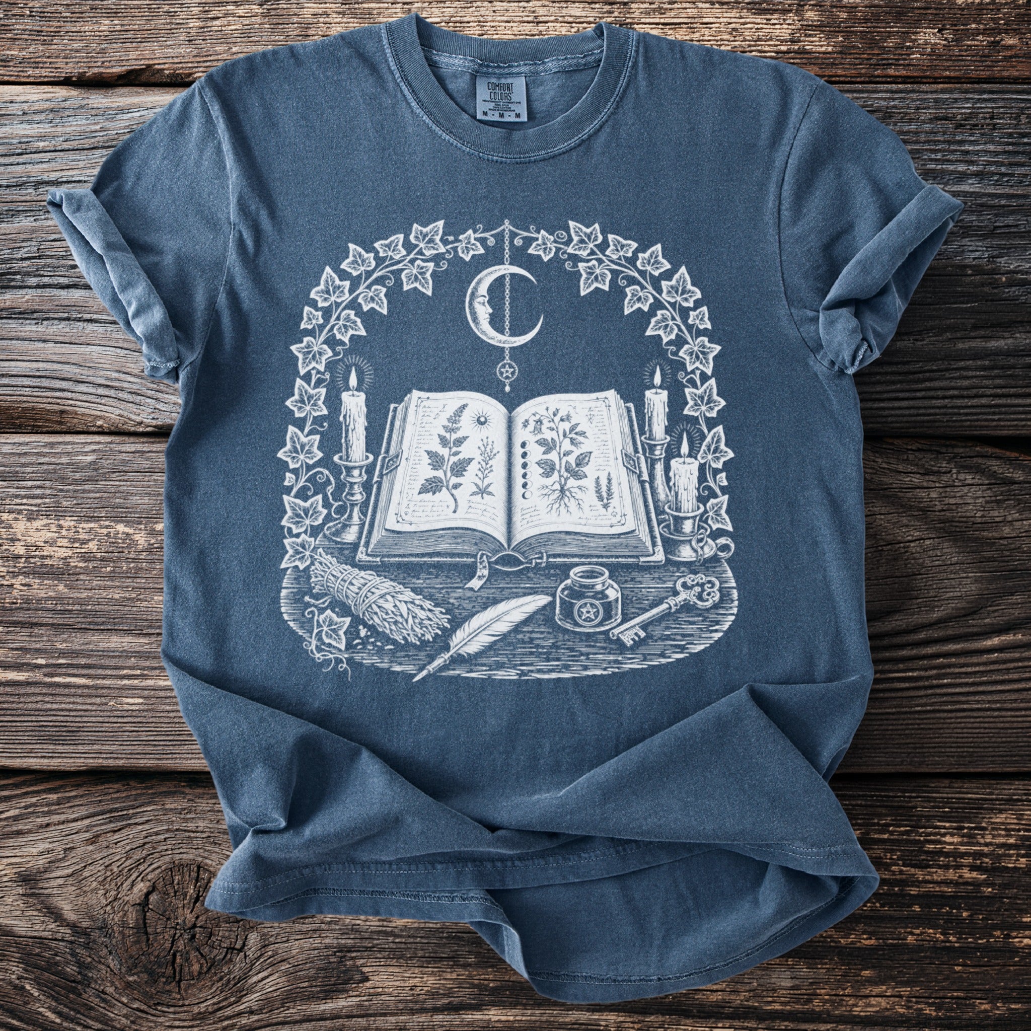 T-shirt with occult graphic: open book, candles, moon, quill, inkwell, key, and herbs.