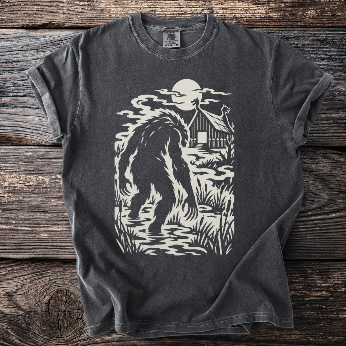 Bigfoot silhouette wading in a misty swamp in front of a cabin under the moon.