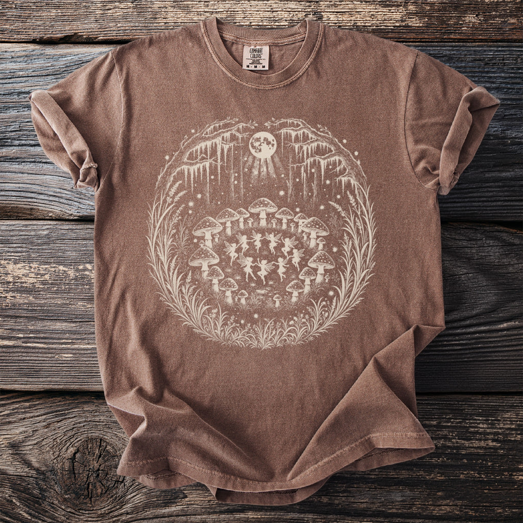 Brown t-shirt with a circular graphic of fairies dancing among mushrooms under a full moon.