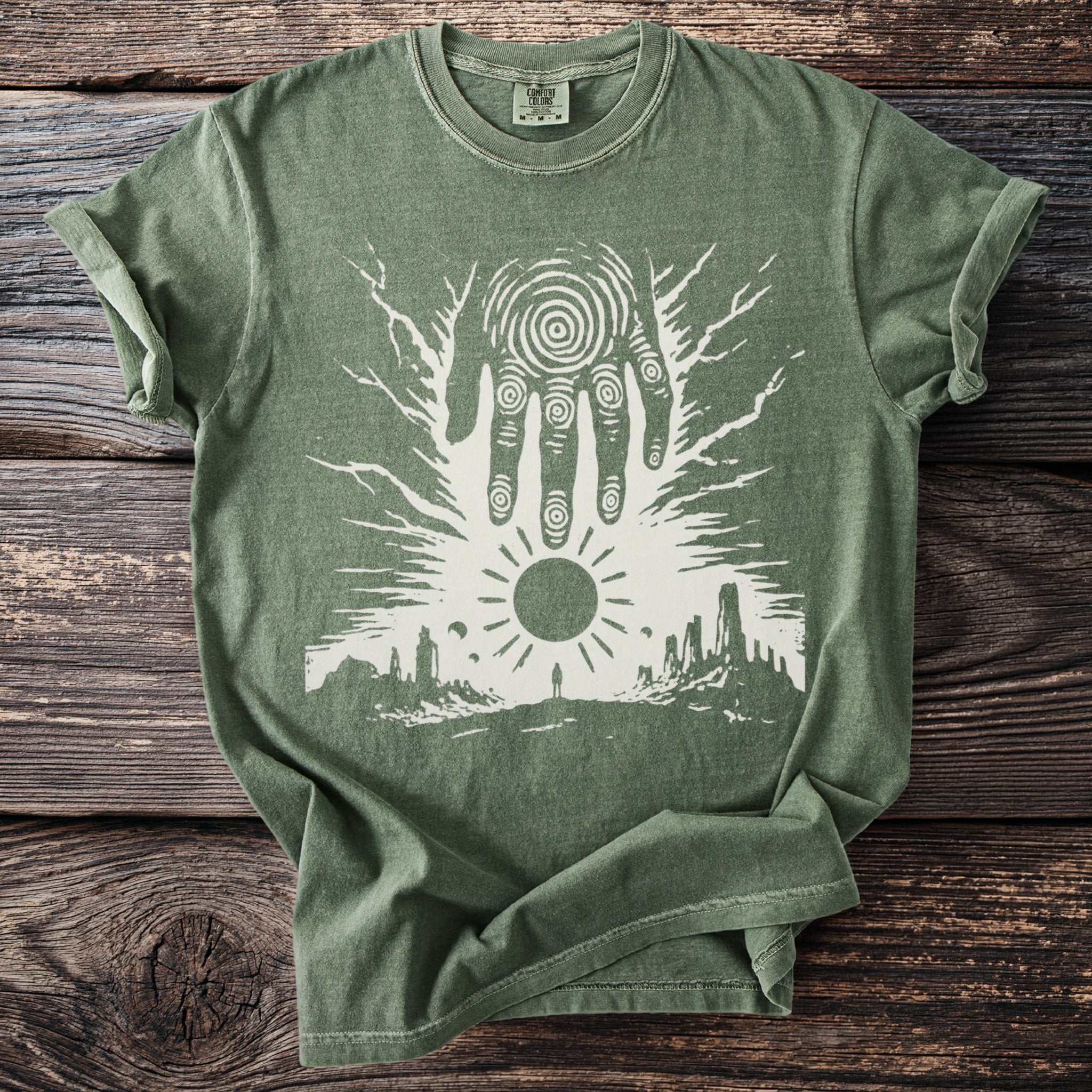 Green t-shirt with white graphic of hand, sun, and solitary figure on landscape.