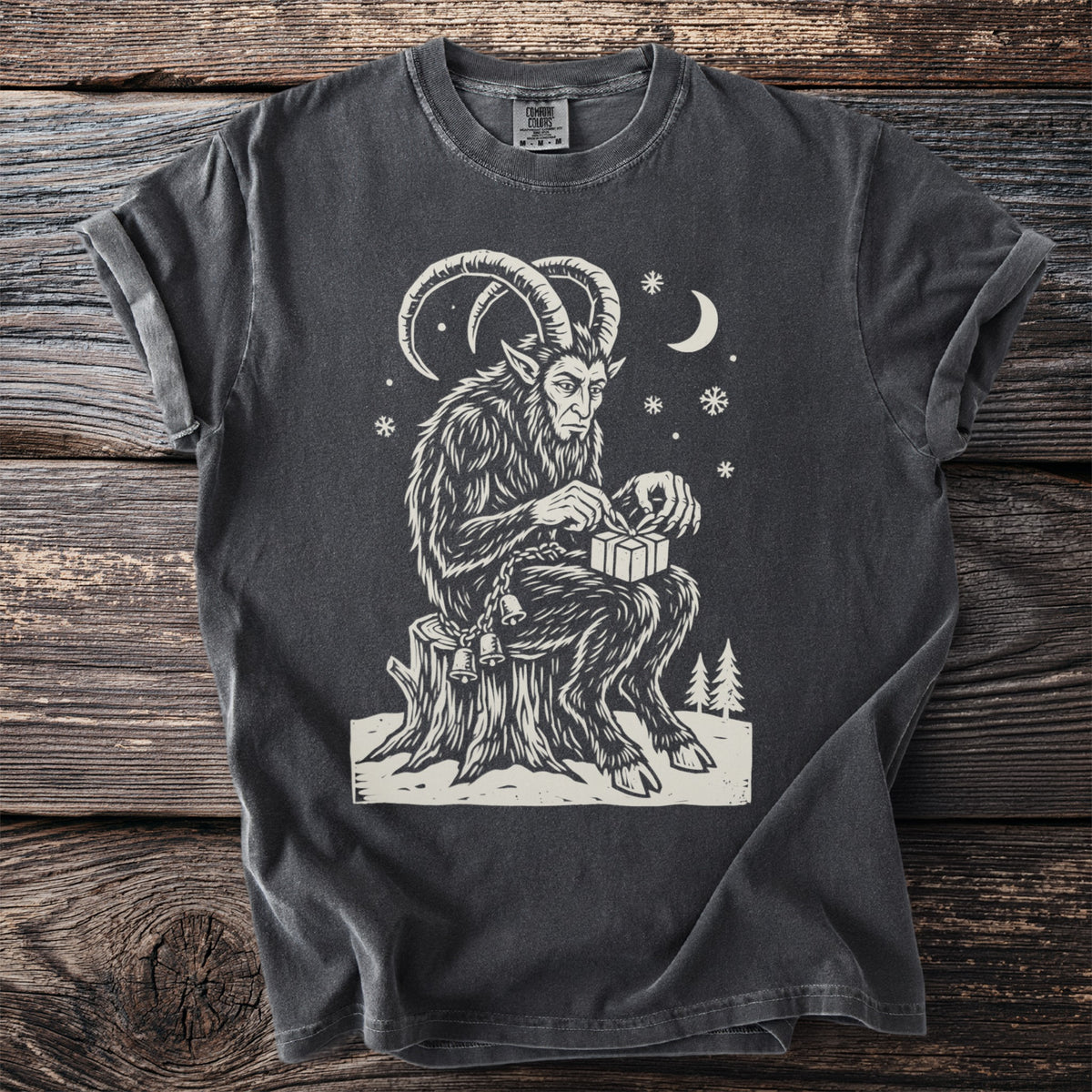 Pepper gray t-shirt with a cream folk-cut print: Krampus sits on a stump in the snow, carefully tying a small present with ribbon.