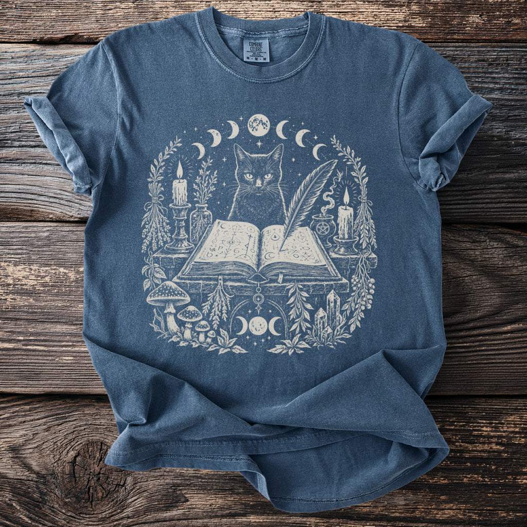 Blue t-shirt with mystical cat, open book, candles, and moon phases print.