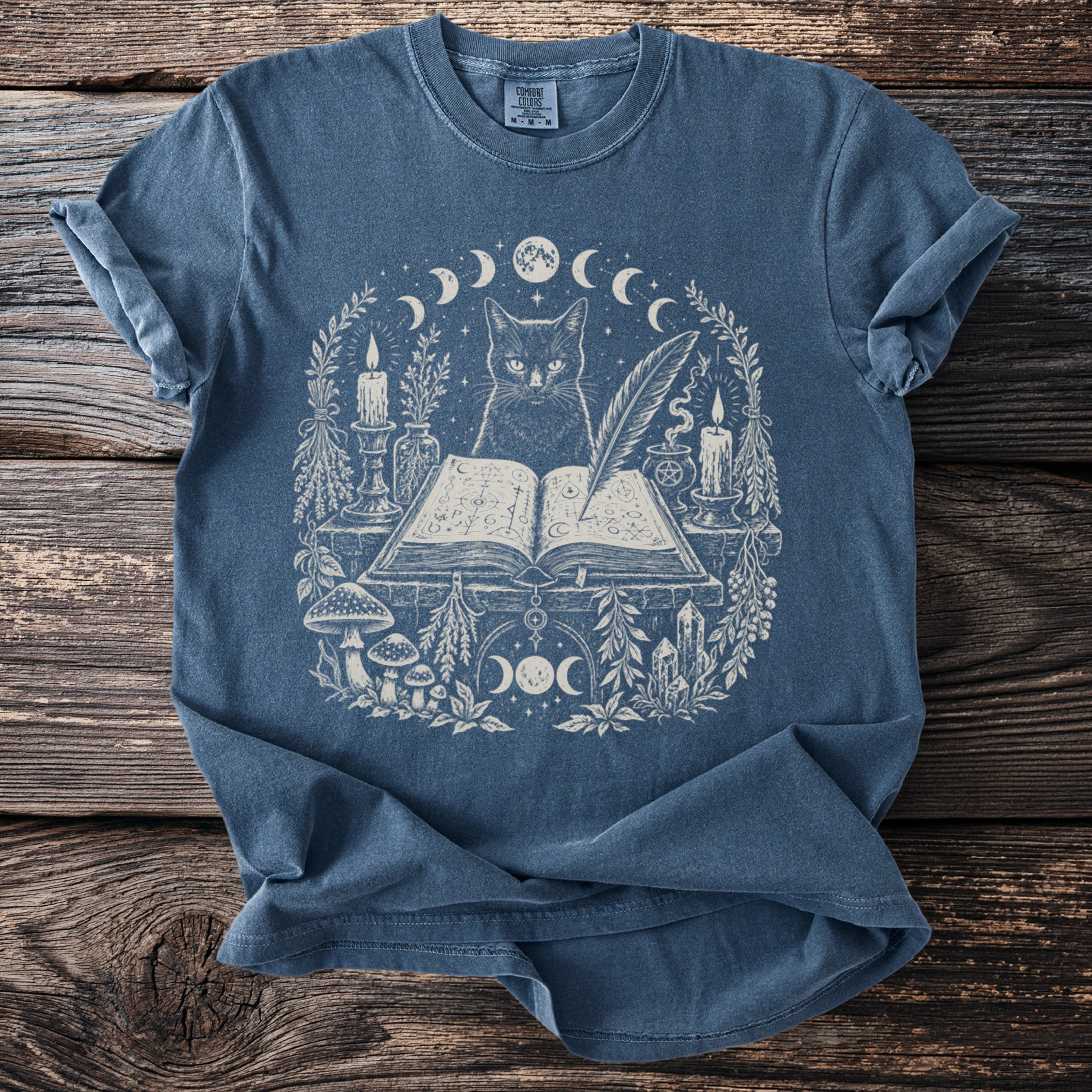 Blue t-shirt with mystical cat, open book, candles, and moon phases print.