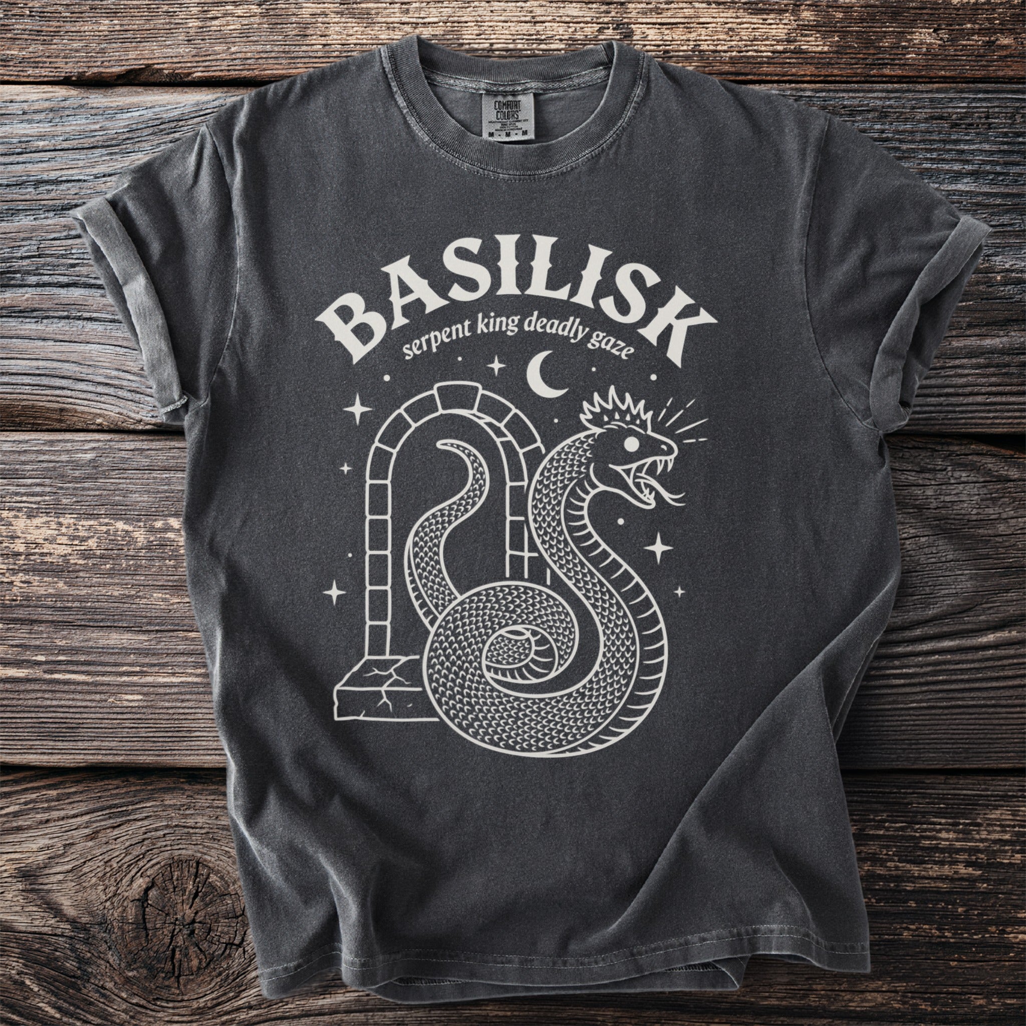 Dark grey t-shirt with white "BASILISK serpent king deadly gaze" text and snake graphic.