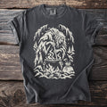 Dark t-shirt with a cream graphic of a witch stirring a cauldron in a snowy forest.
