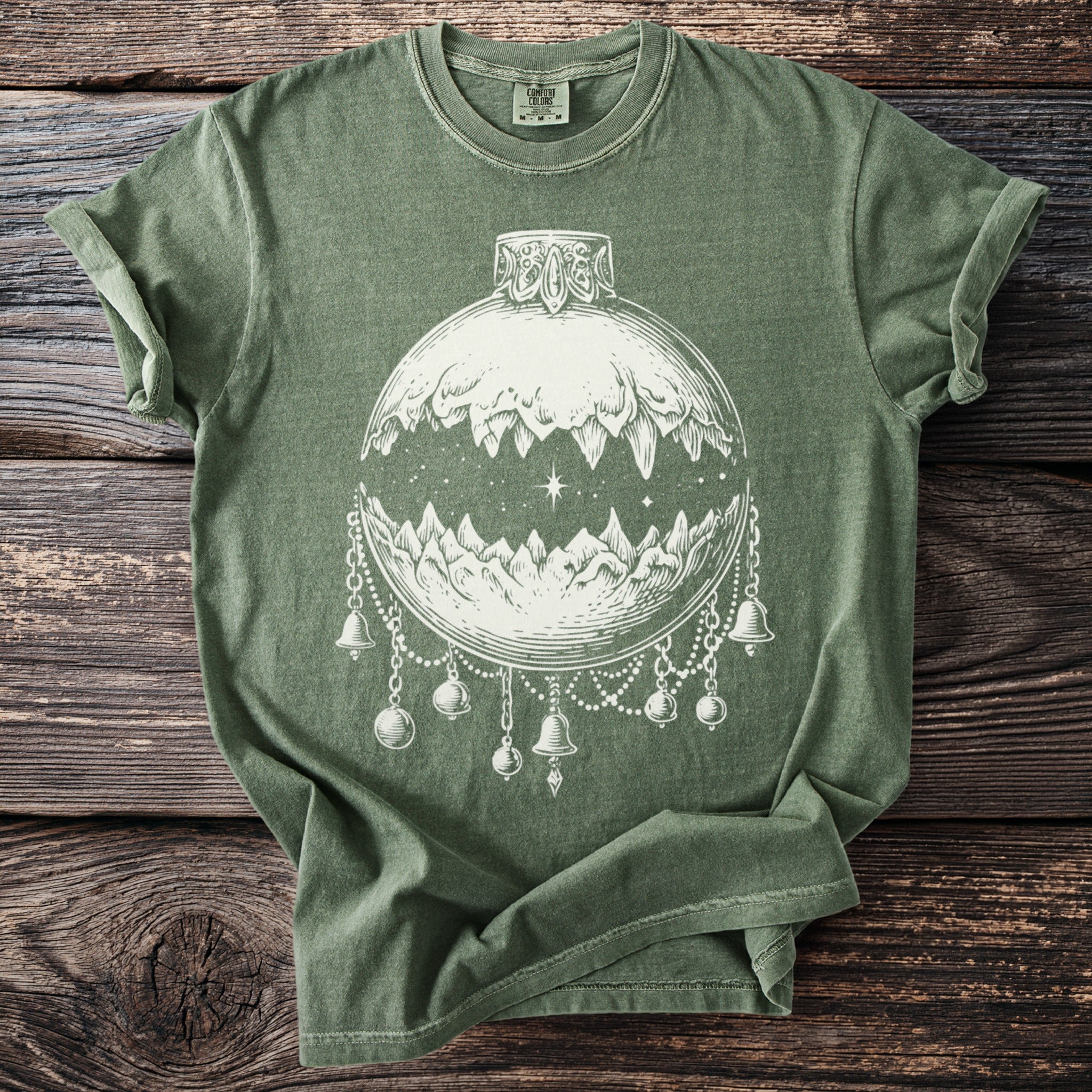 Green t-shirt with white line art of an ornate ornament with mountains and bells.