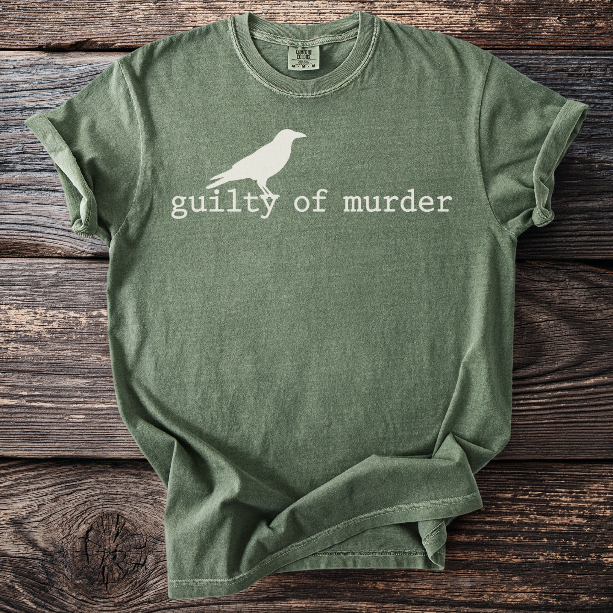 Green t-shirt with white crow graphic and text "guilty of murder."
