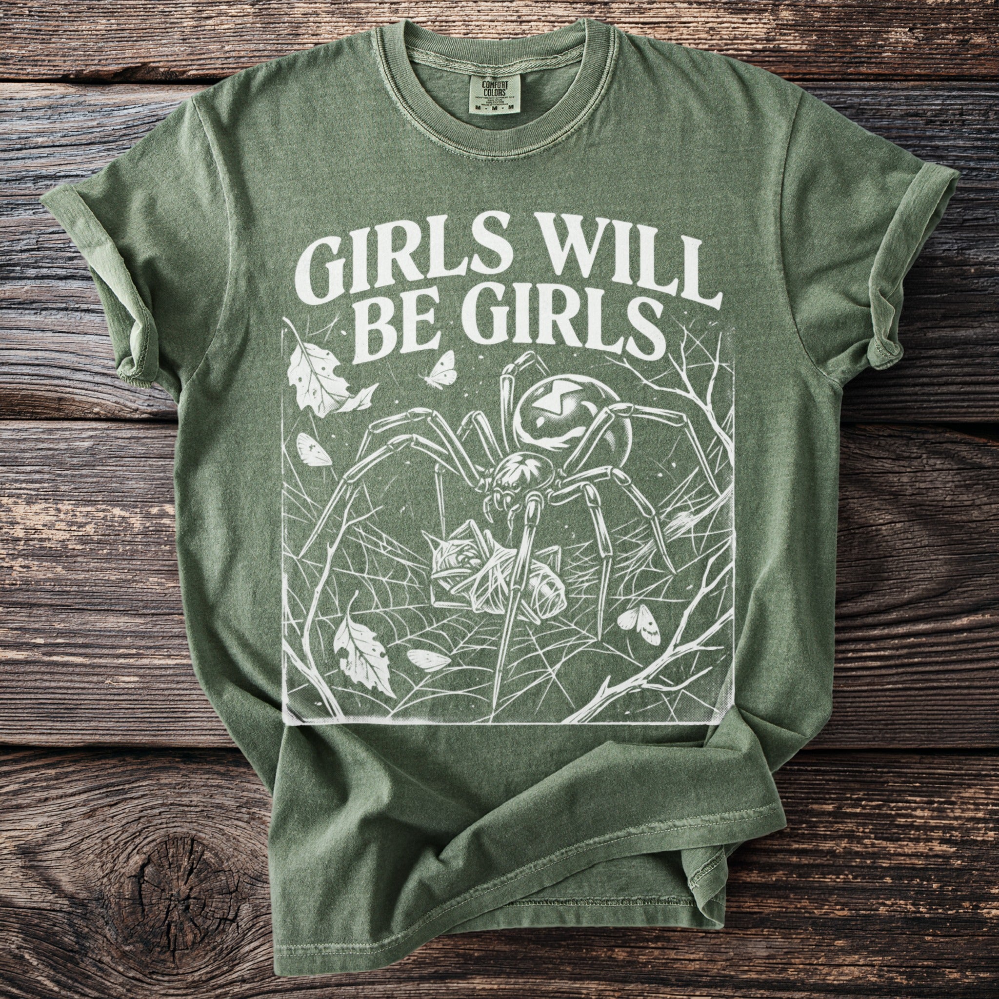 Green t-shirt with white graphic of spider, web, moths, and text "GIRLS WILL BE GIRLS".