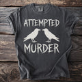 Dark t-shirt with white text "ATTEMPTED MURDER" and two white ravens.