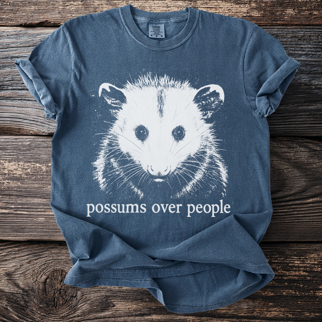 Blue t-shirt with white graphic of a possum and text "possums over people."