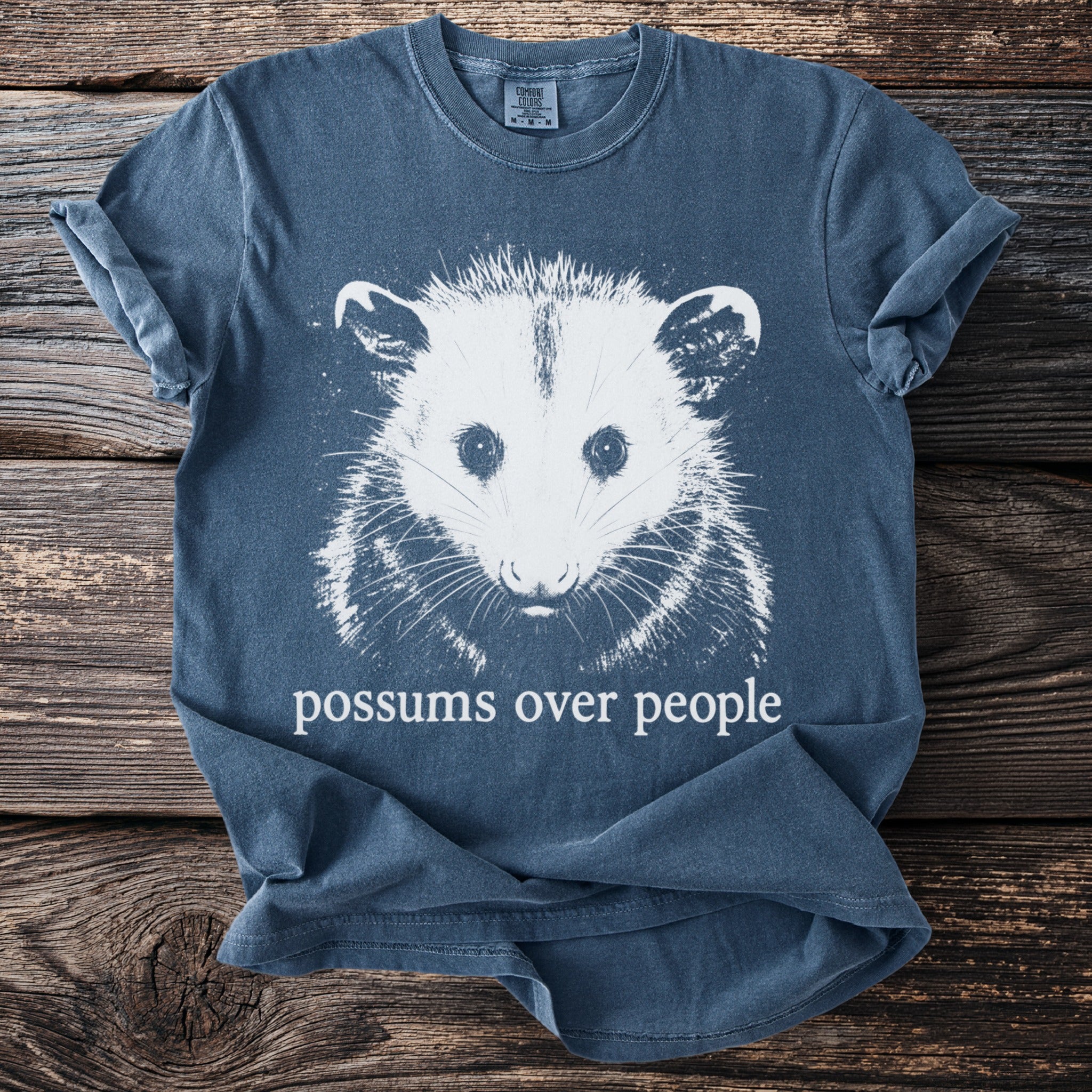 Blue t-shirt with white graphic of a possum and text "possums over people."