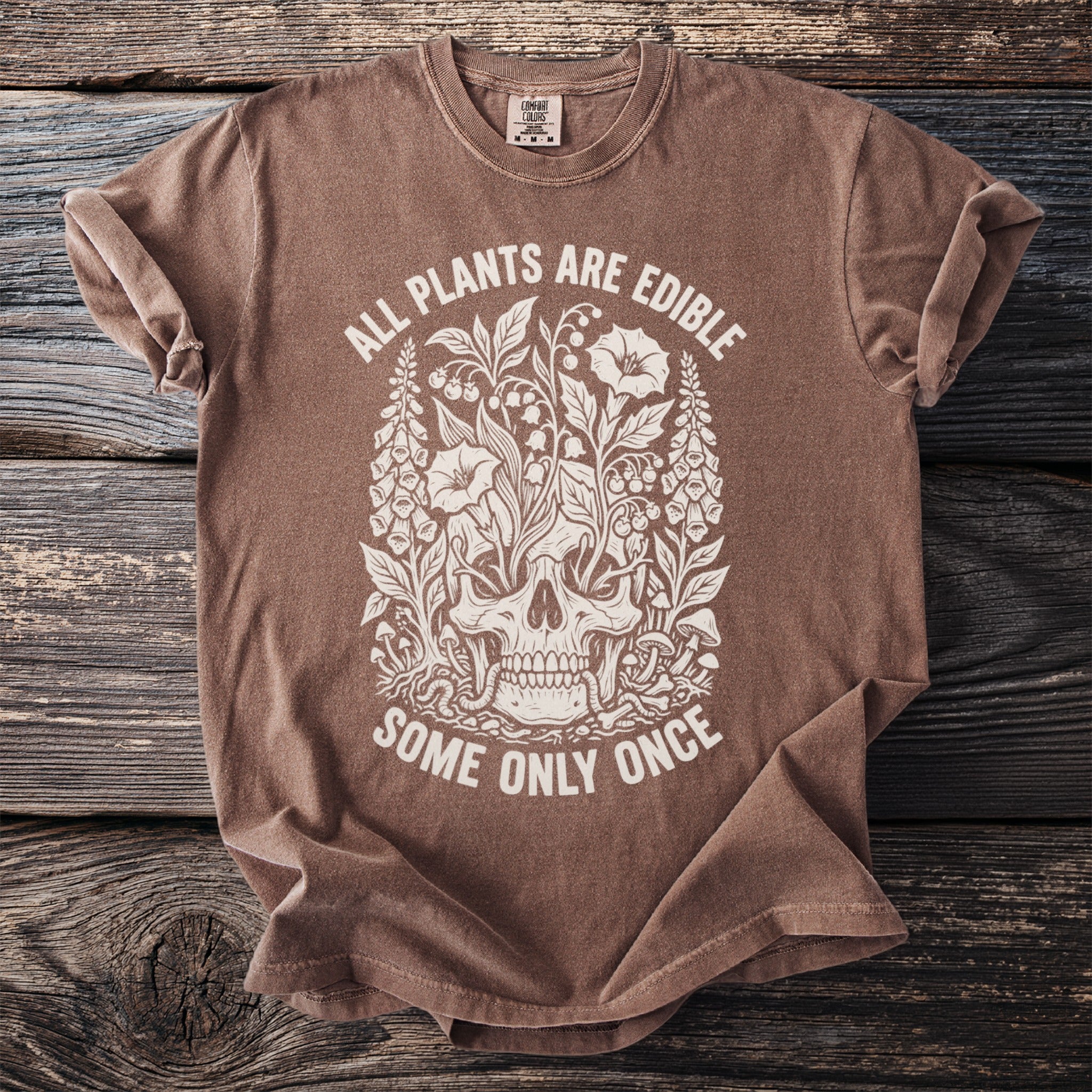 Brown t-shirt with white text and illustration of skull surrounded by plants.