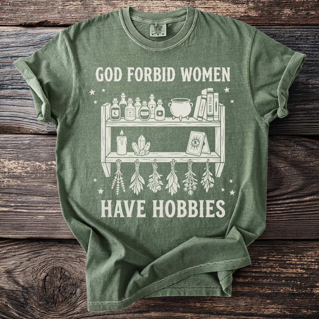 Green t-shirt with white graphic text "GOD FORBID WOMEN HAVE HOBBIES" and witchy imagery.