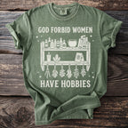 Green t-shirt with white graphic text "GOD FORBID WOMEN HAVE HOBBIES" and witchy imagery.