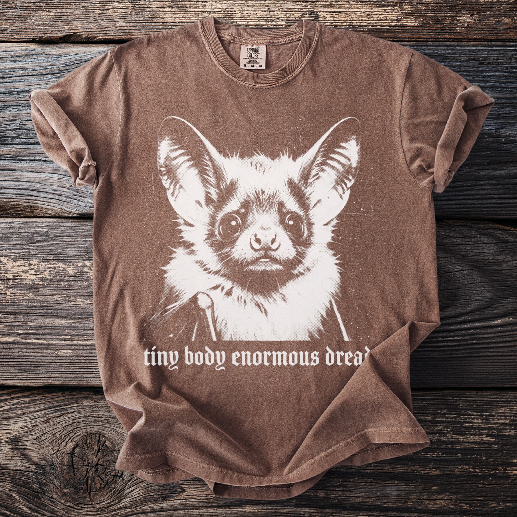 Brown t-shirt with a front graphic of a bat face and text "tiny body enormous dread".