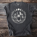 Dark t-shirt with white graphic of cats, crystals, moon phases, and floral wreath.