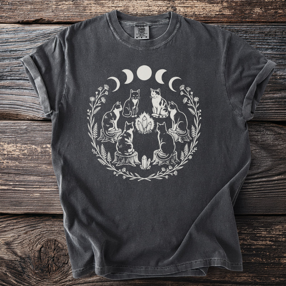 Dark t-shirt with white graphic of cats, crystals, moon phases, and floral wreath.