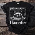 Black t-shirt with a stark white graphic of a raccoon peeking from a drainpipe, text reads "i have rabies".